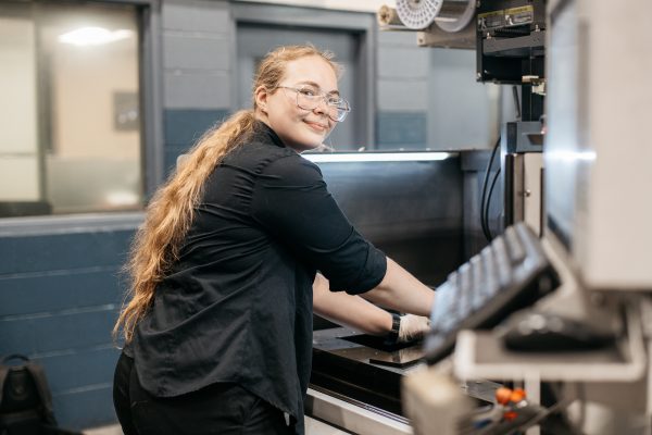 Pre-Apprentice Cynthia Cooper Operating an EDM Machine at Cavalier Tool and Manufacturing Ltd. She is looking back and smiling at the camera.
